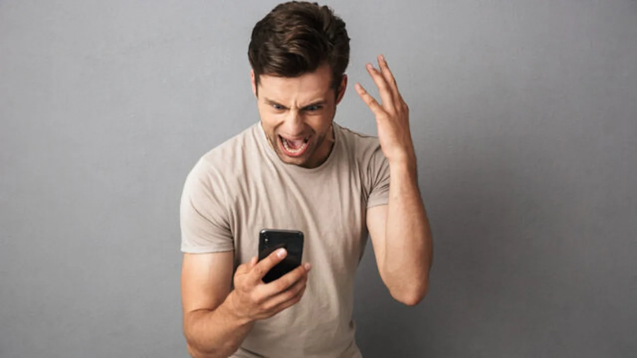 A man looking annoyed at his phone with one hand on his head