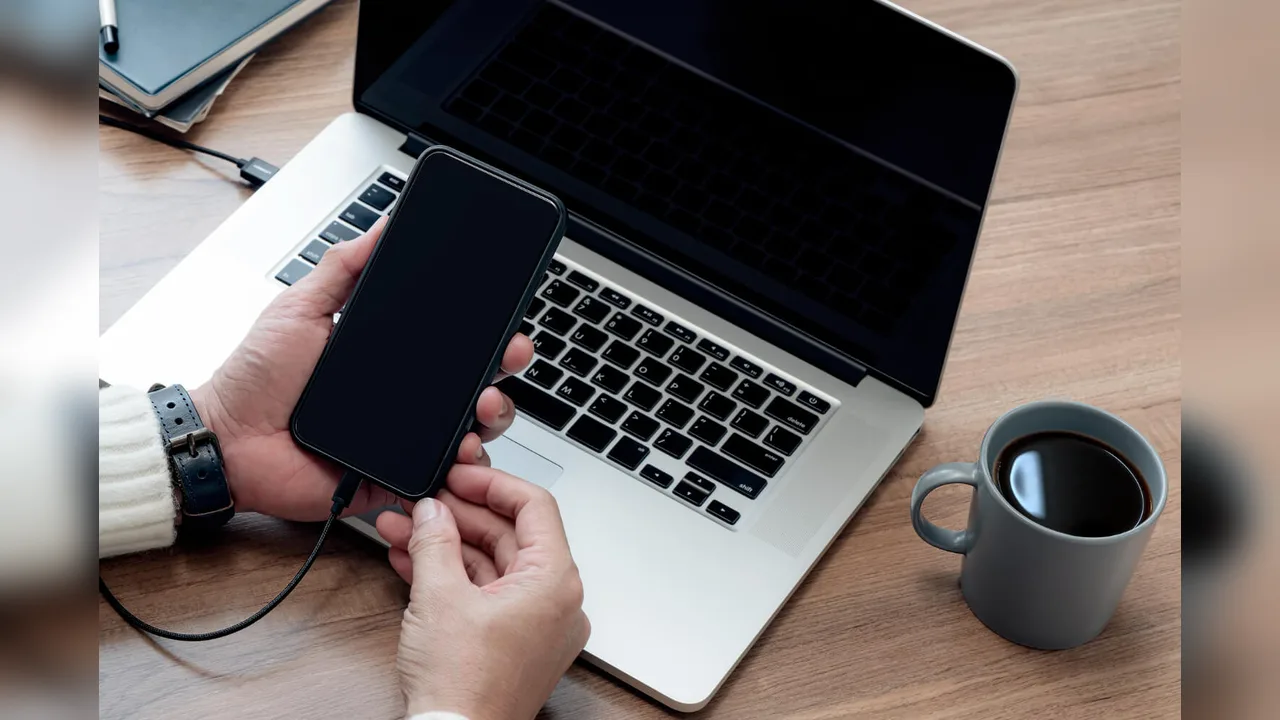 Hands holding a phone next to a laptop and a mug of coffee on a desk