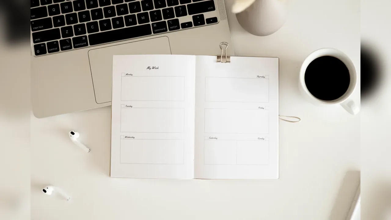 An open planner notebook beside a laptop and a cup of coffee on a white desk